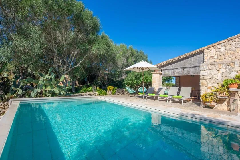 An outdoor swimming pool beside a stone building, with loungers and a shaded patio.