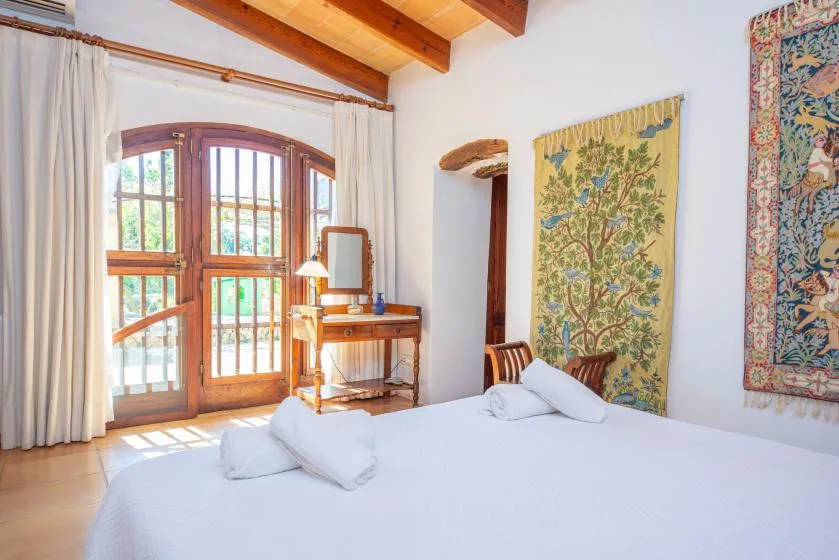 A bedroom with a large bed, wooden-framed windows, and wall hangings.