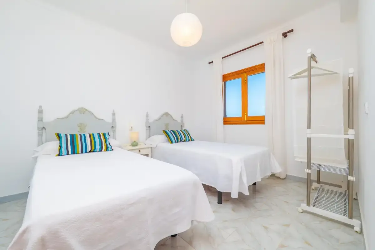 A bright bedroom with two beds and an orange-framed window.