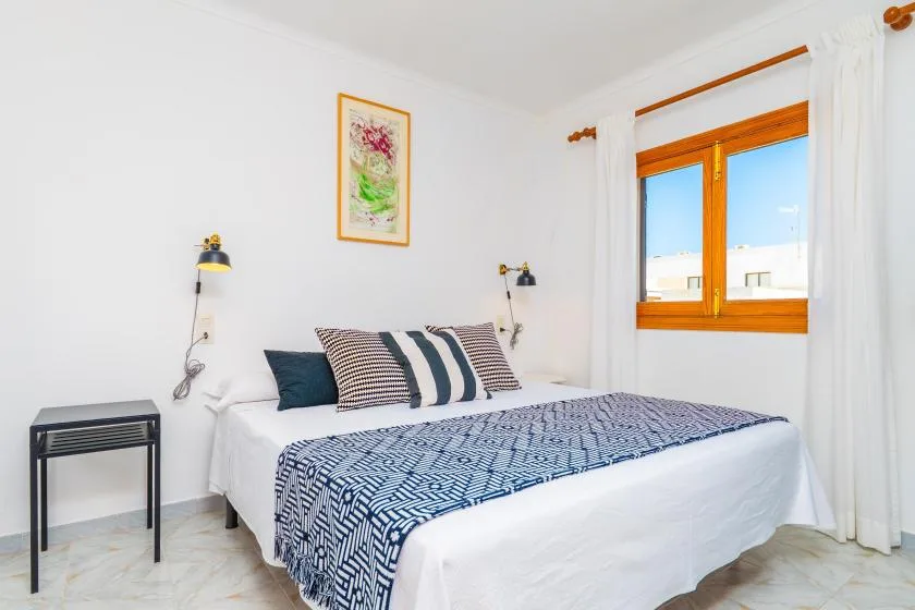 A bright bedroom with a double bed, patterned bedding, and a wooden-framed window.