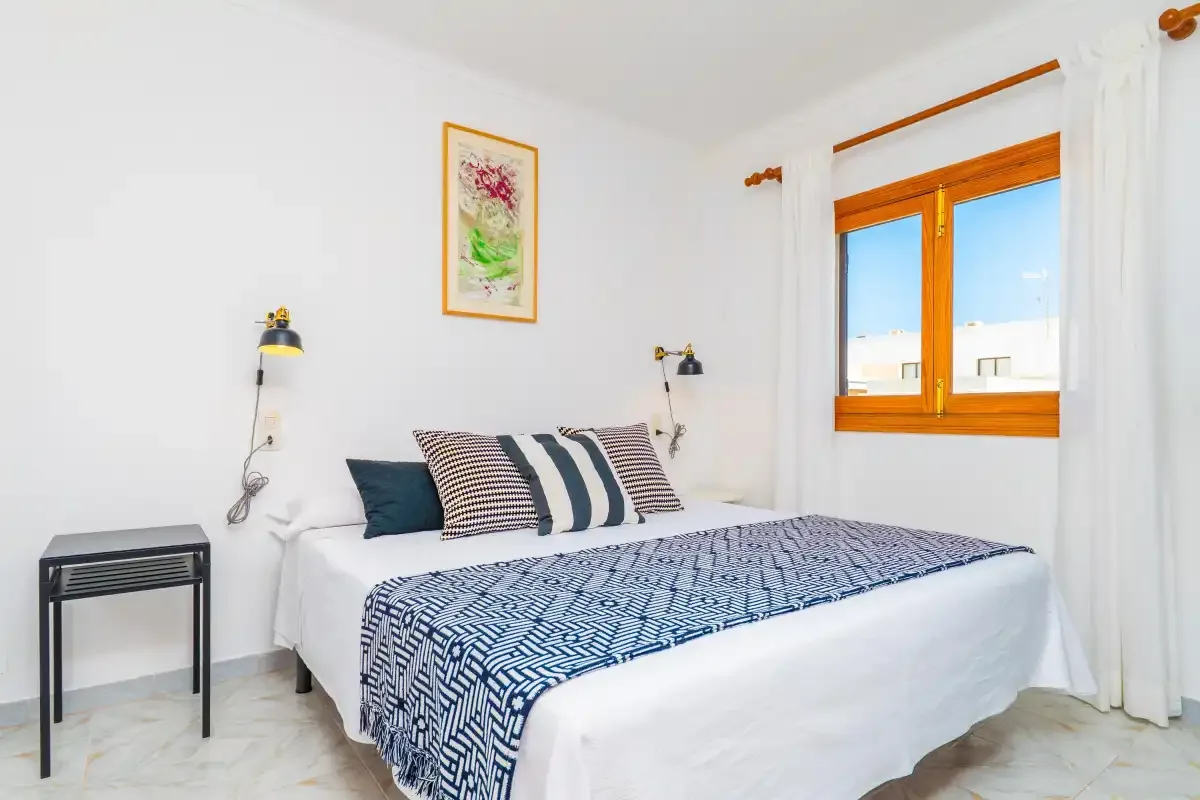 A bright bedroom with a bed beside a wooden-framed window.