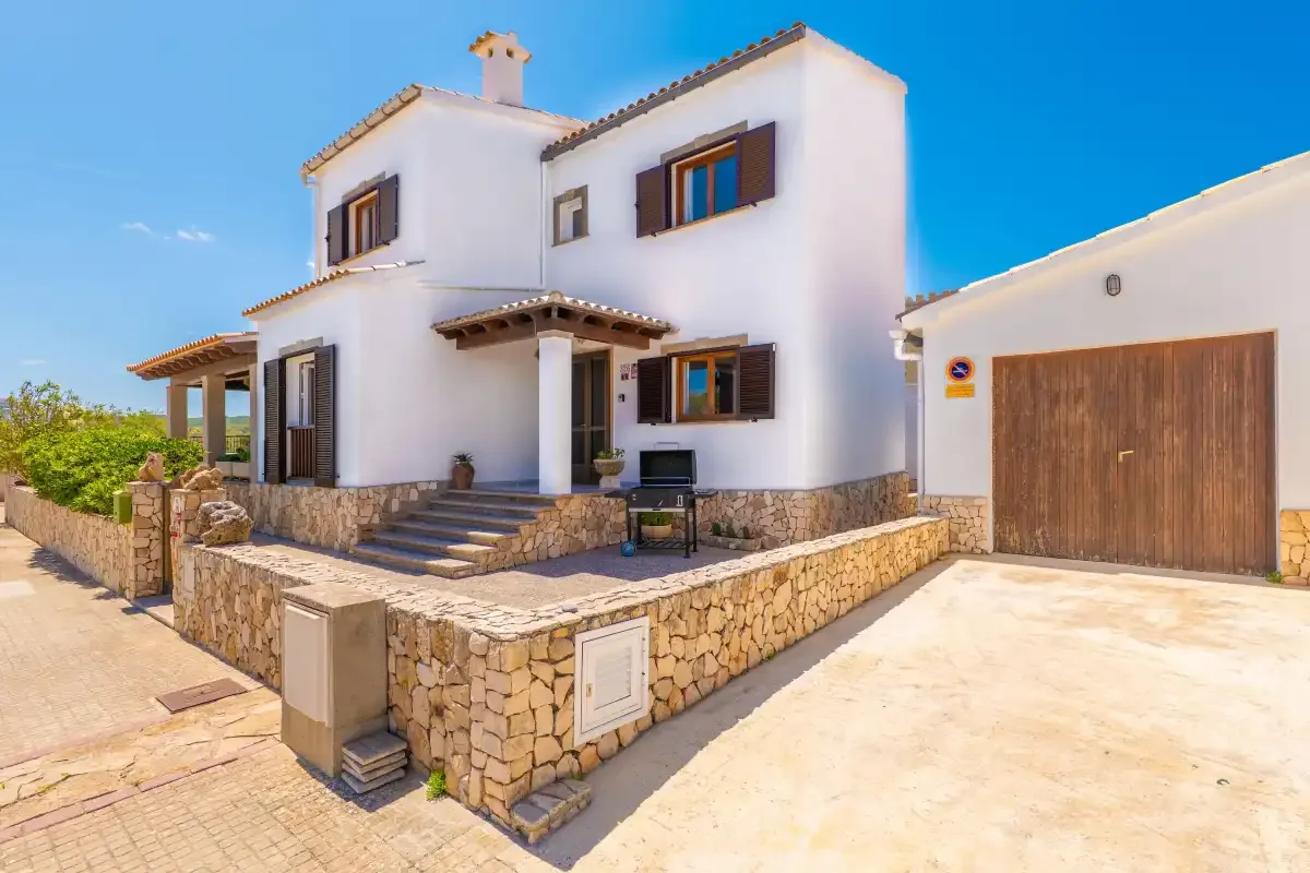 A white two-story house with a stone terrace and adjoining garage.