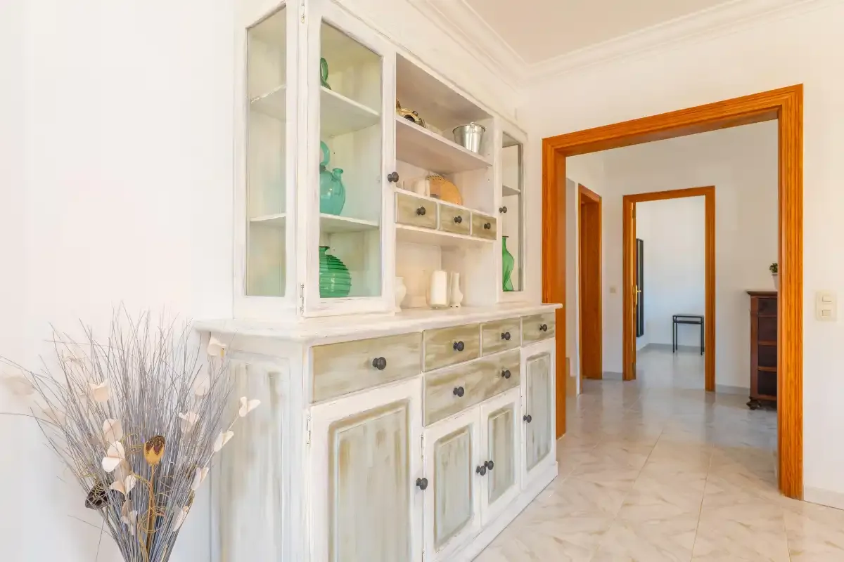 A bright hallway features a white display cabinet and open doorways.