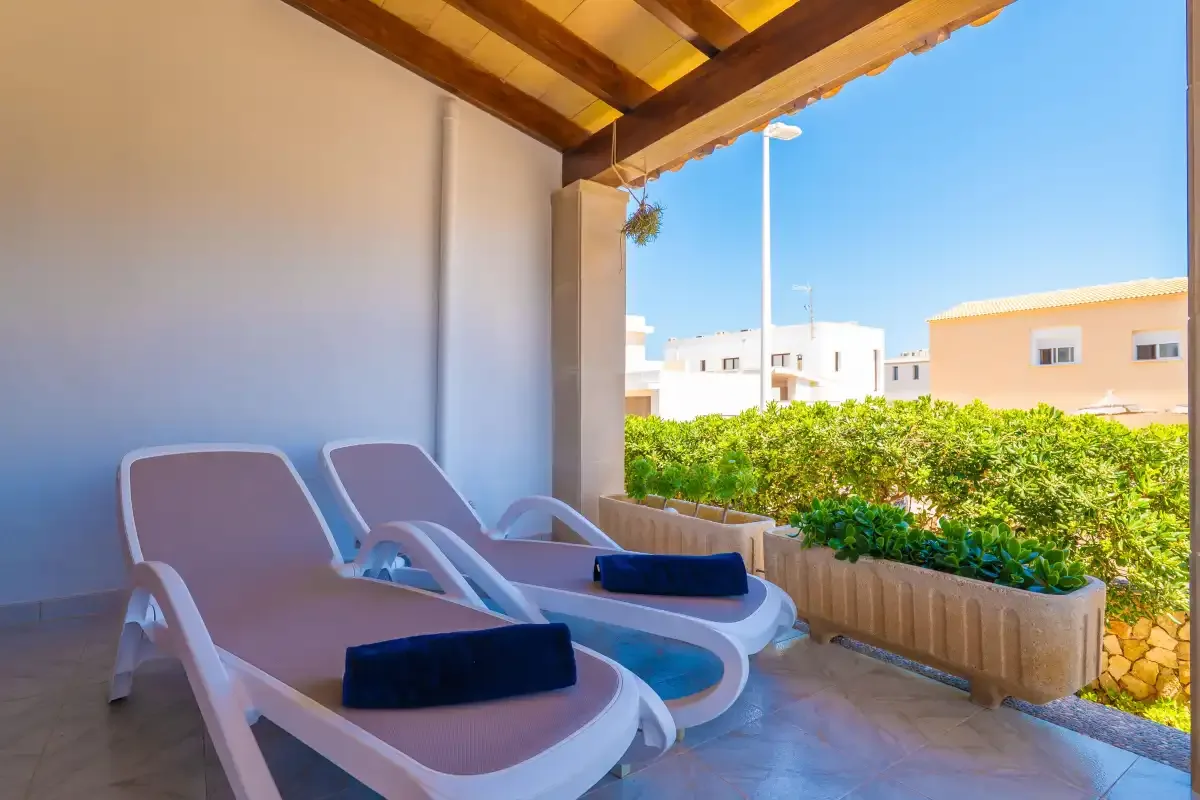 A covered patio with reclining loungers beside a row of leafy plants.