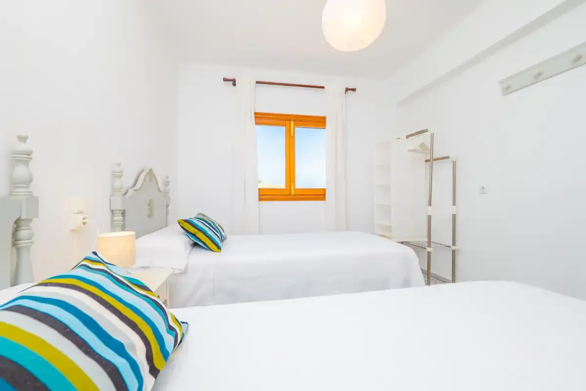 A bright bedroom with white bedding and a window with wooden trim.
