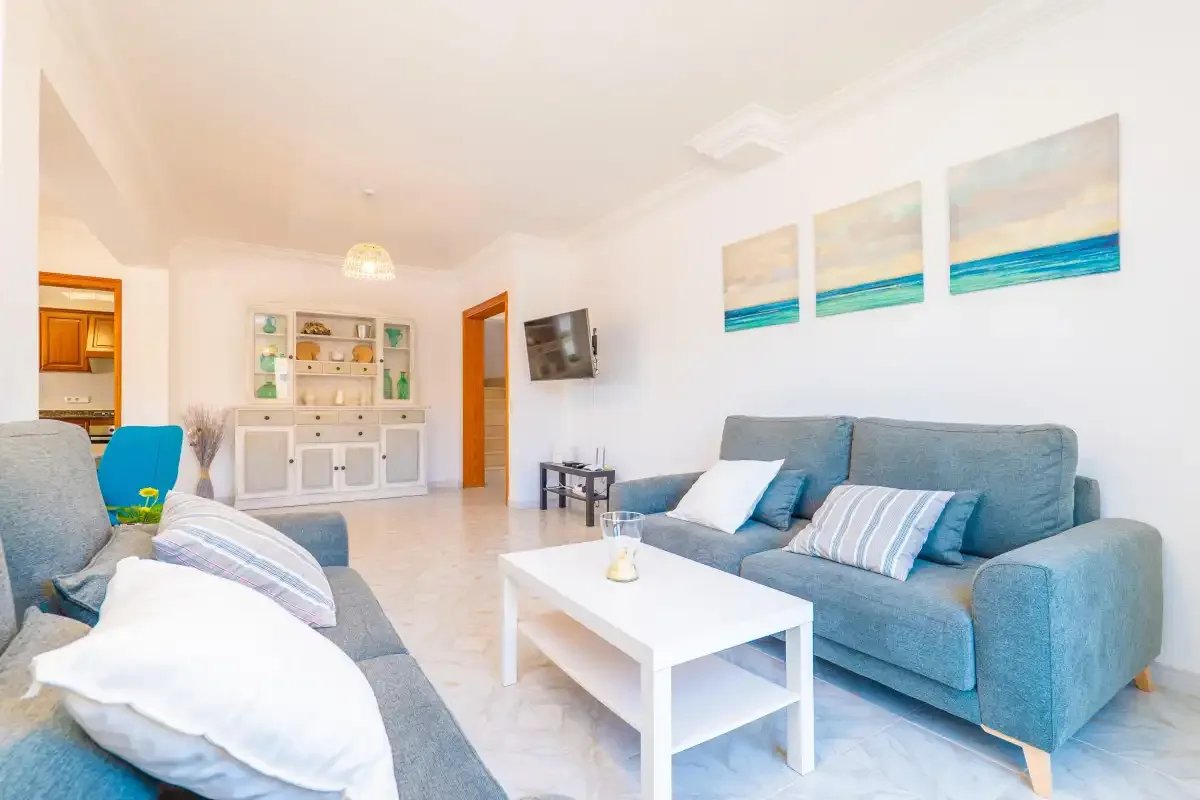 A bright living room with blue seating, a white coffee table, and coastal wall art.