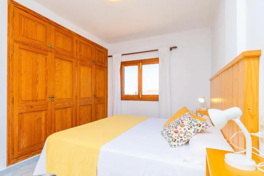 A bedroom with a bed, wooden wardrobes, and a window.