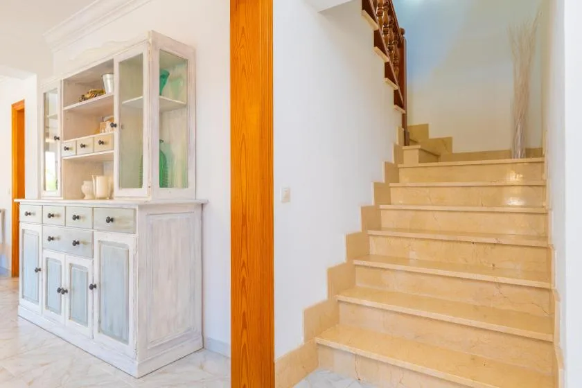 A bright interior shows a pale display cabinet beside a staircase.