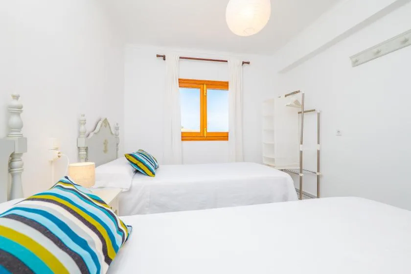 A bright bedroom with white bedding and a window with orange trim.