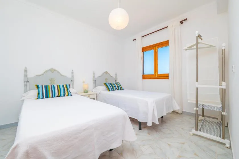 A bright bedroom with two beds dressed in white beside a window.