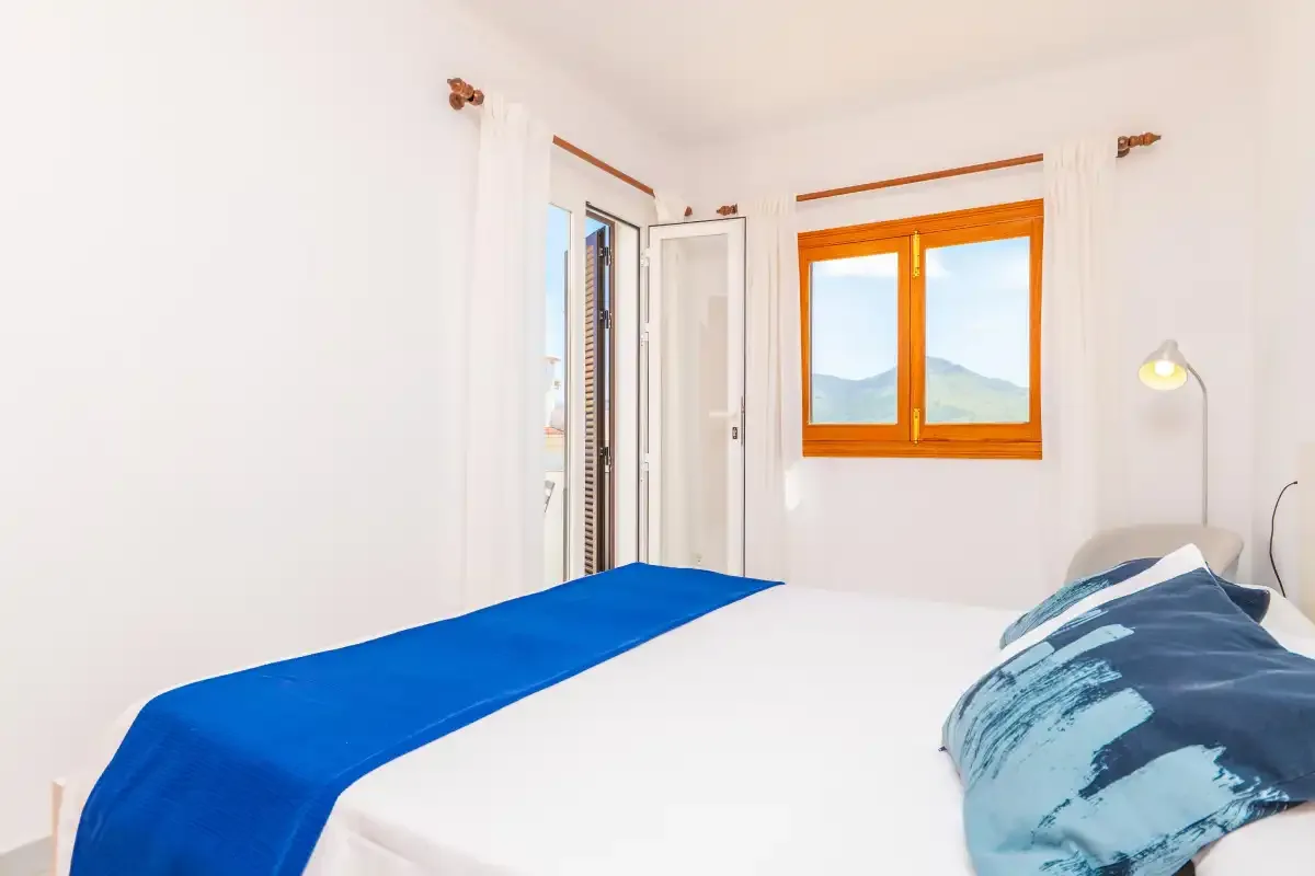 A bright bedroom with a bed and windows overlooking distant hills.