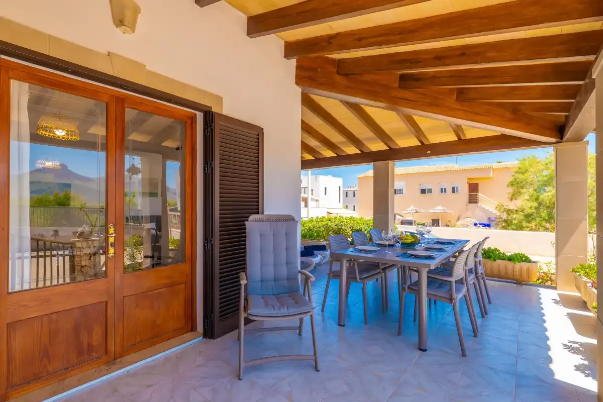 A covered outdoor dining area with a table and seating beside glass doors.