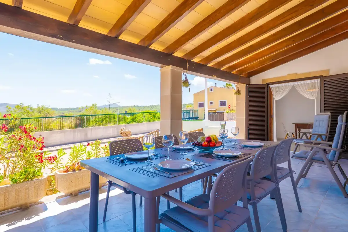 A covered outdoor dining area with a set table and chairs overlooking greenery.