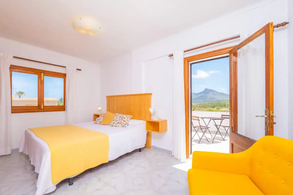 A bright bedroom with a bed and an open door leading to a balcony.