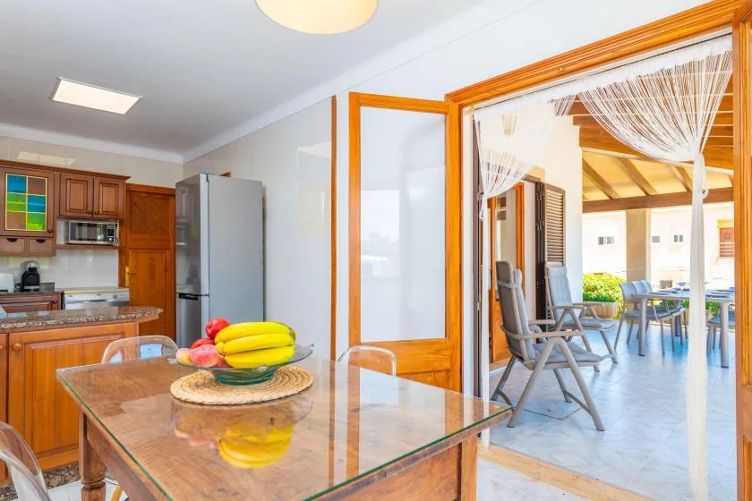 A kitchen and dining area open through wooden doors to a covered patio with seating.