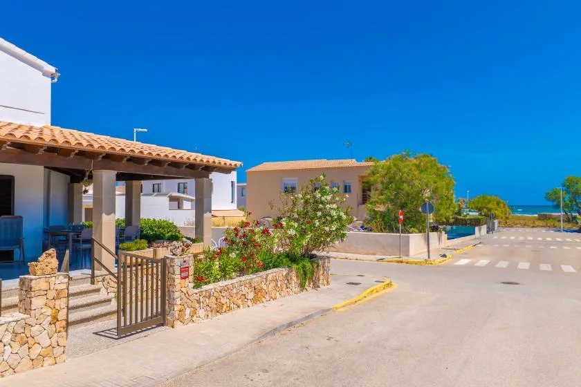 A sunny street beside low-rise buildings, with a planted garden and the sea visible in the distance.