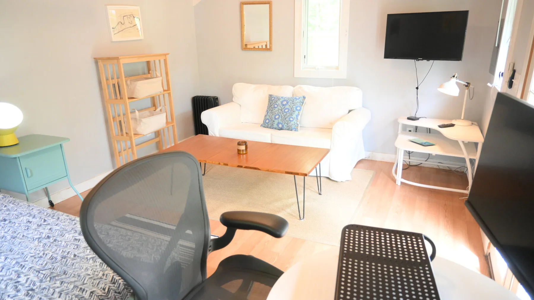 A bright living room with a white sofa, wooden coffee table, and wall-mounted television.