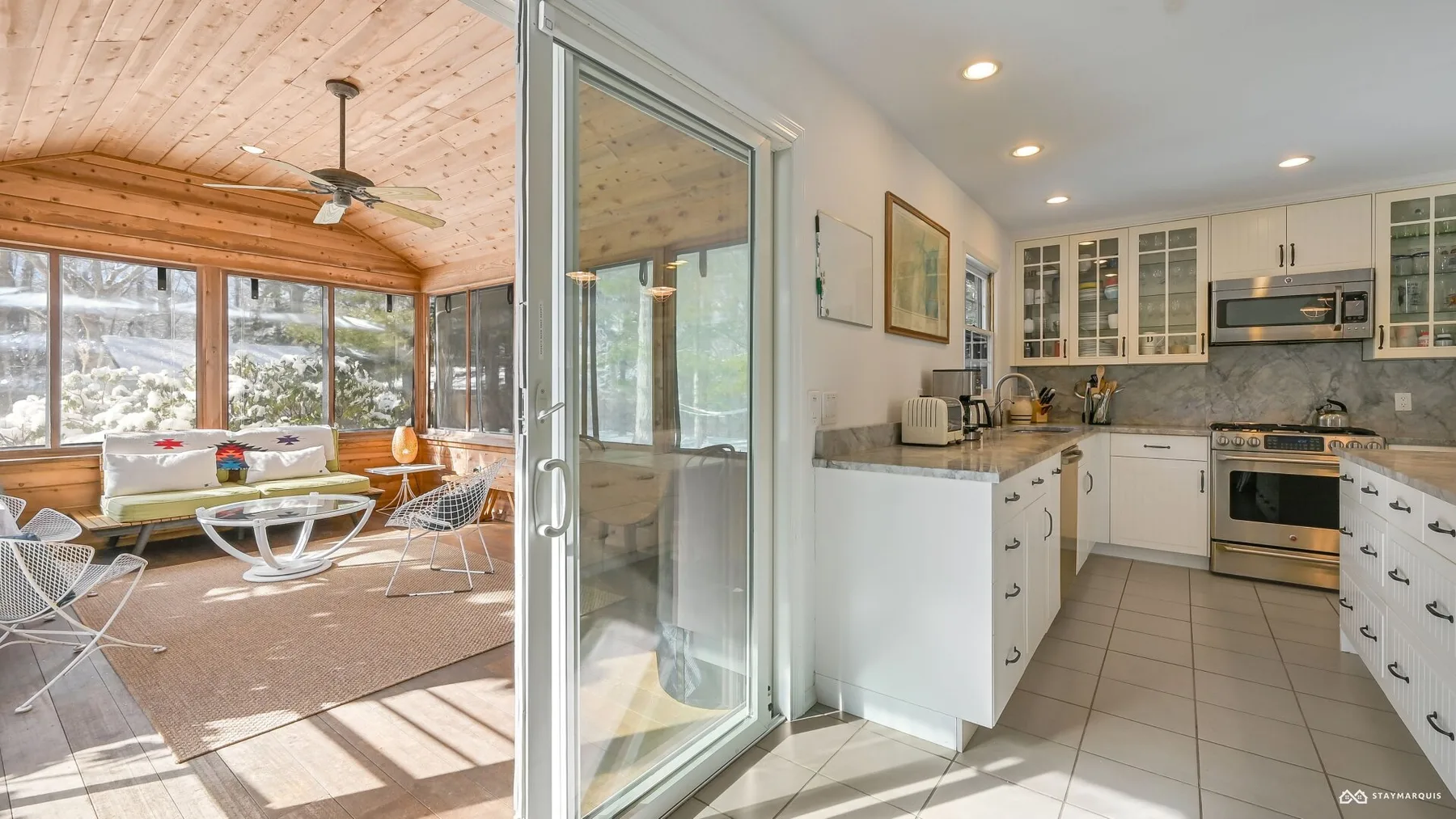 A bright kitchen opens onto a sunroom with large windows and seating.