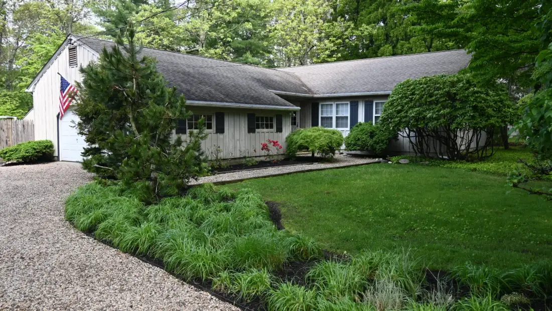 A single-story house stands beside a gravel driveway and landscaped lawn.