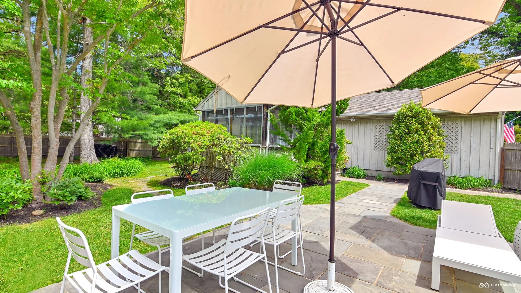 A garden patio has a dining table and chairs beneath a large umbrella.