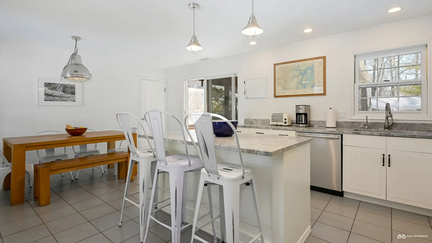 A bright kitchen with a central island, white seating, and a dining table.