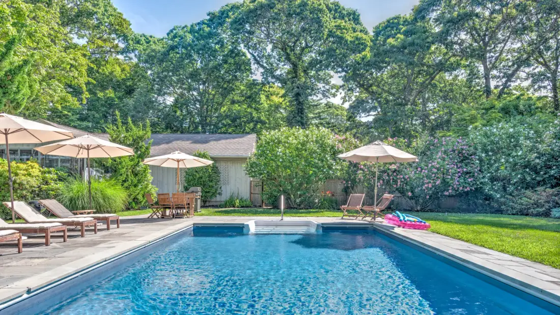 A swimming pool sits in a landscaped garden with lounge seating nearby.