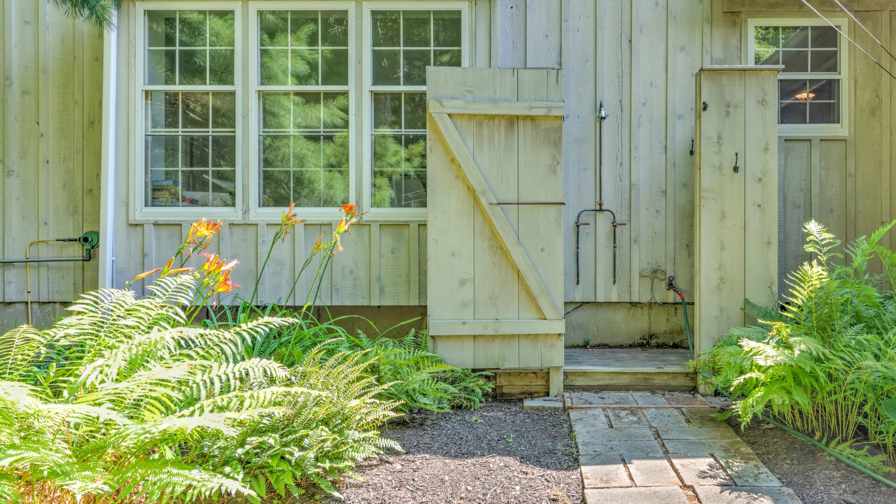 A weathered wooden building with a stone path through lush ferns.
