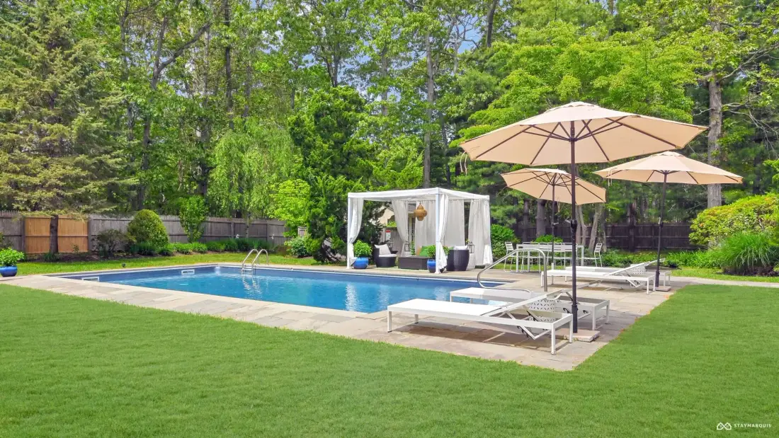Outdoor pool area with lounge seating, umbrellas, and a green lawn.