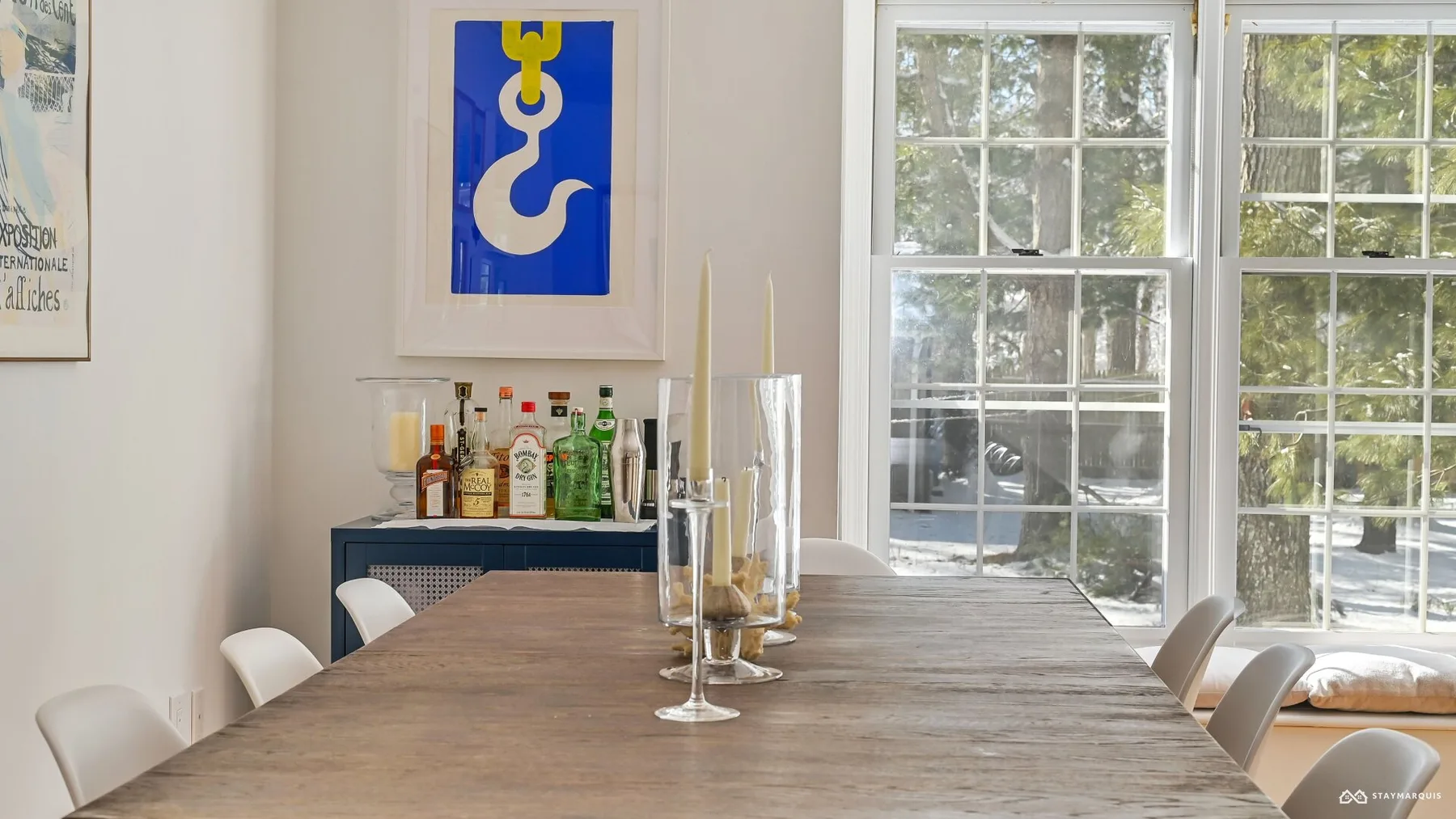 A dining area with a long wooden table and large windows.