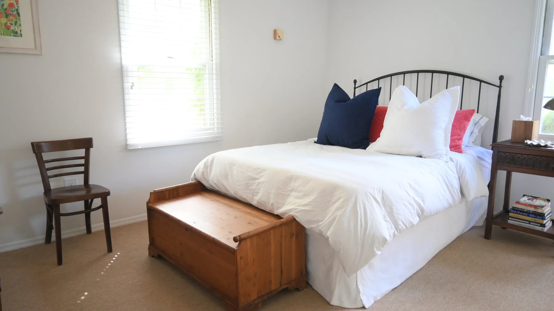 A bedroom with a white bed, dark headboard, and wooden chest at the foot.
