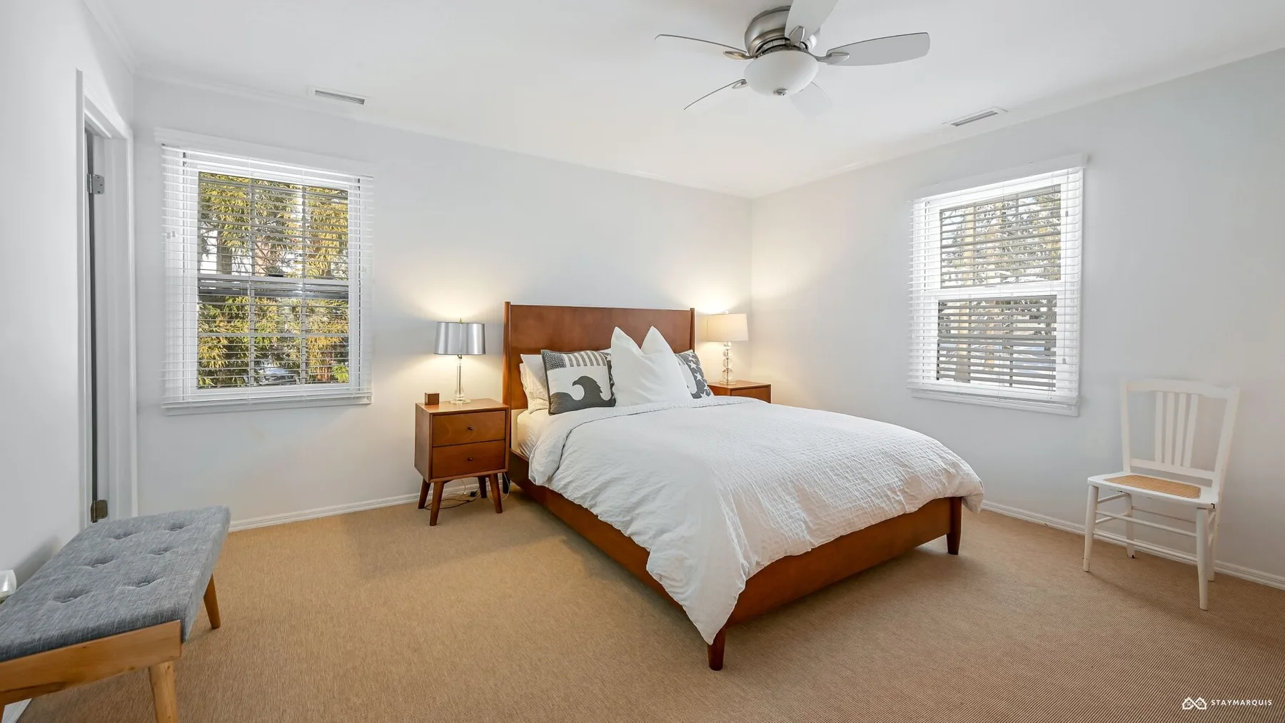 A bedroom with a bed, bedside tables, and windows with blinds.