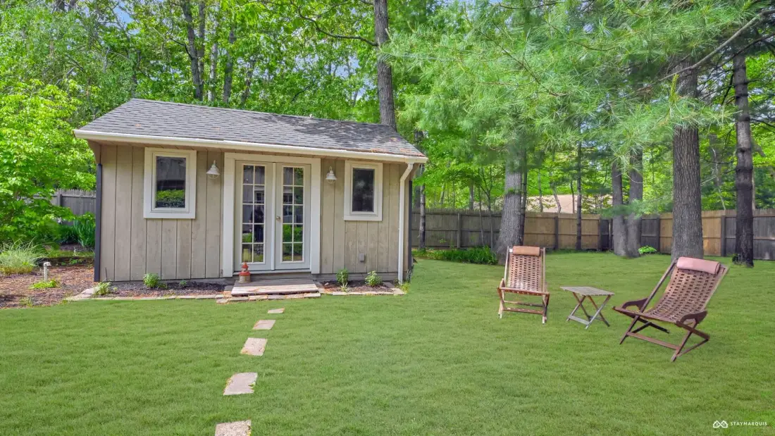 A small garden outbuilding stands beside a lawn with outdoor seating.