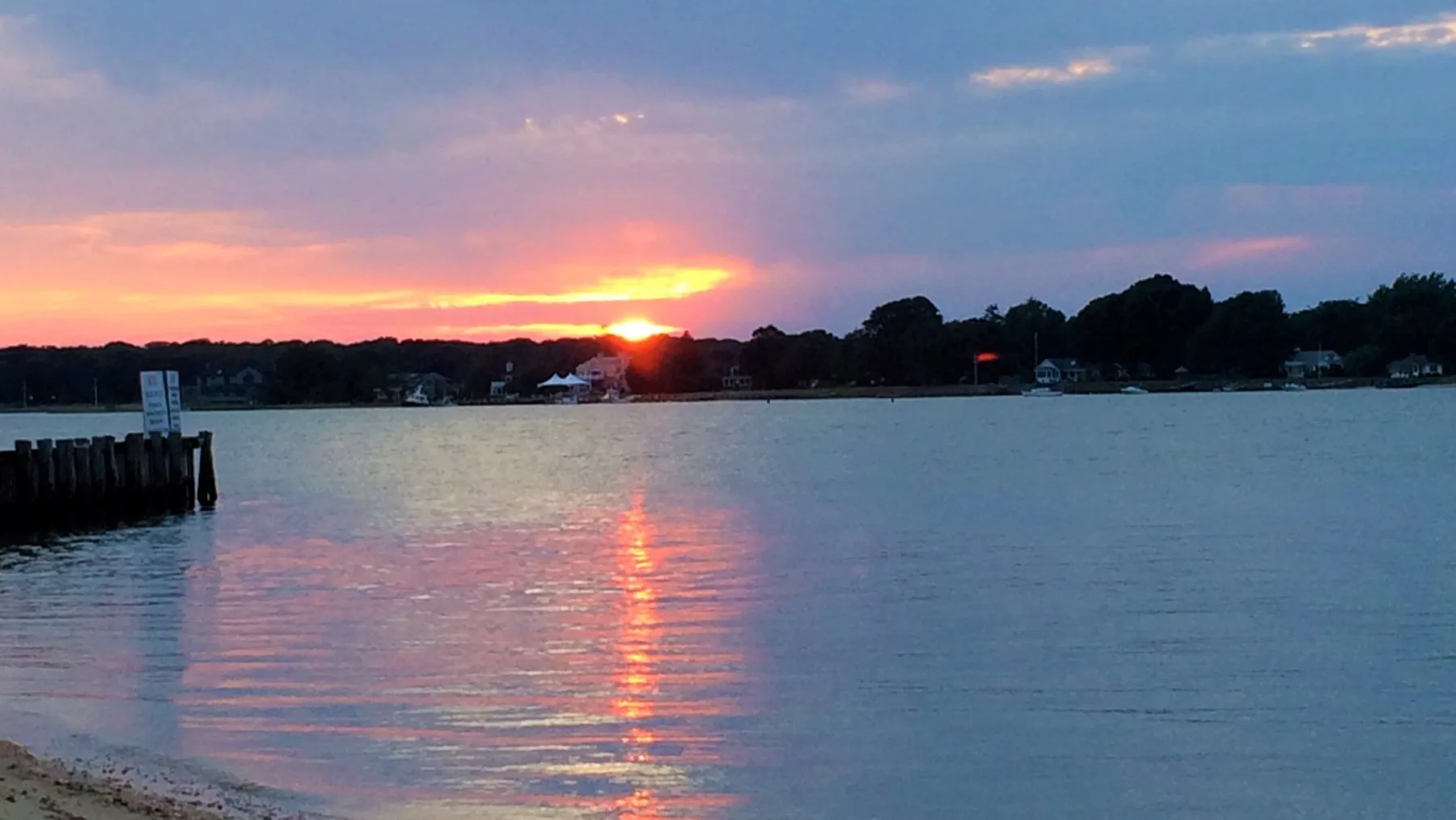 A sunset glows over a calm shoreline, reflecting across the water.