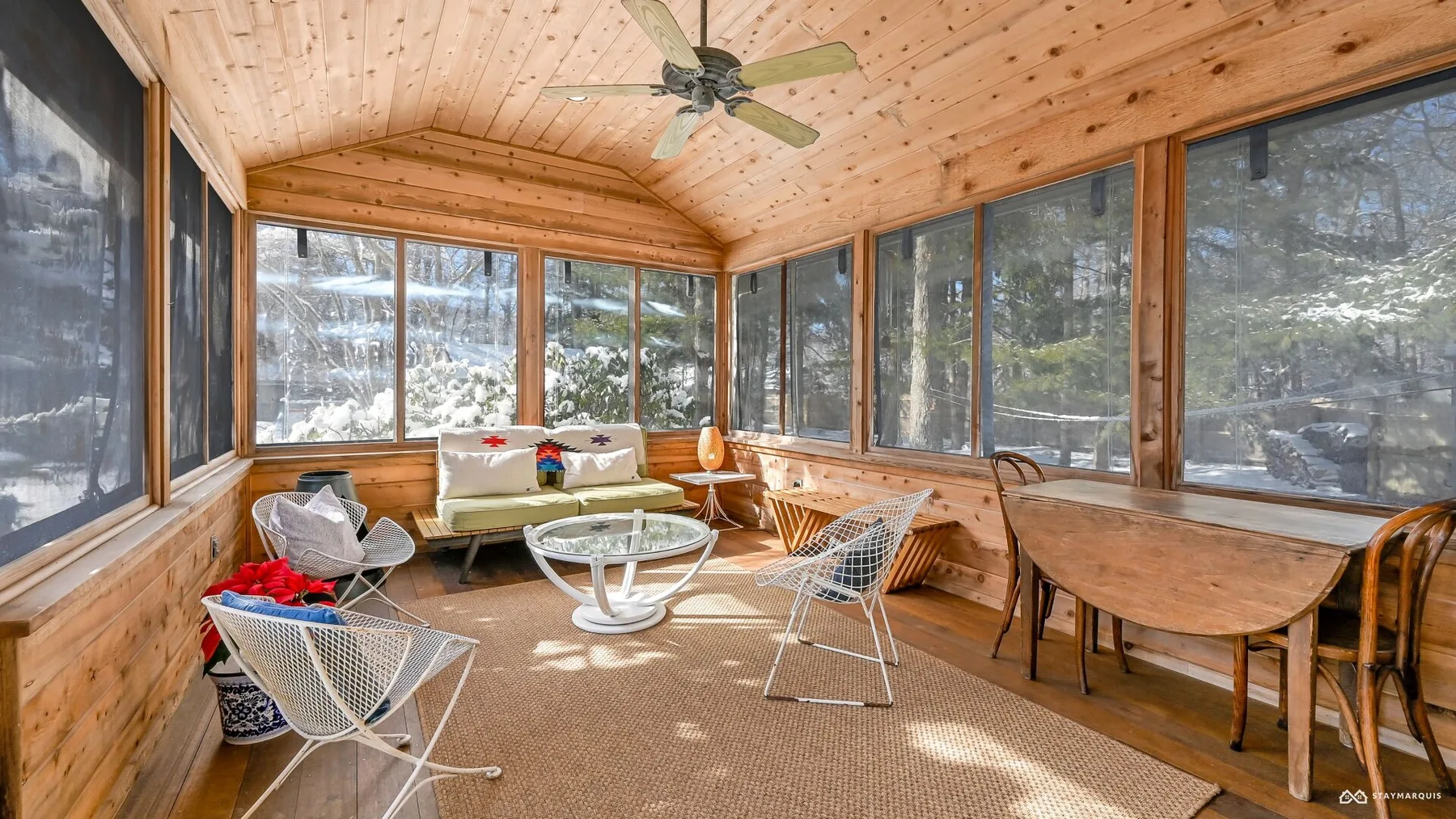 A sunroom with large windows, wood-paneled walls, and casual seating.