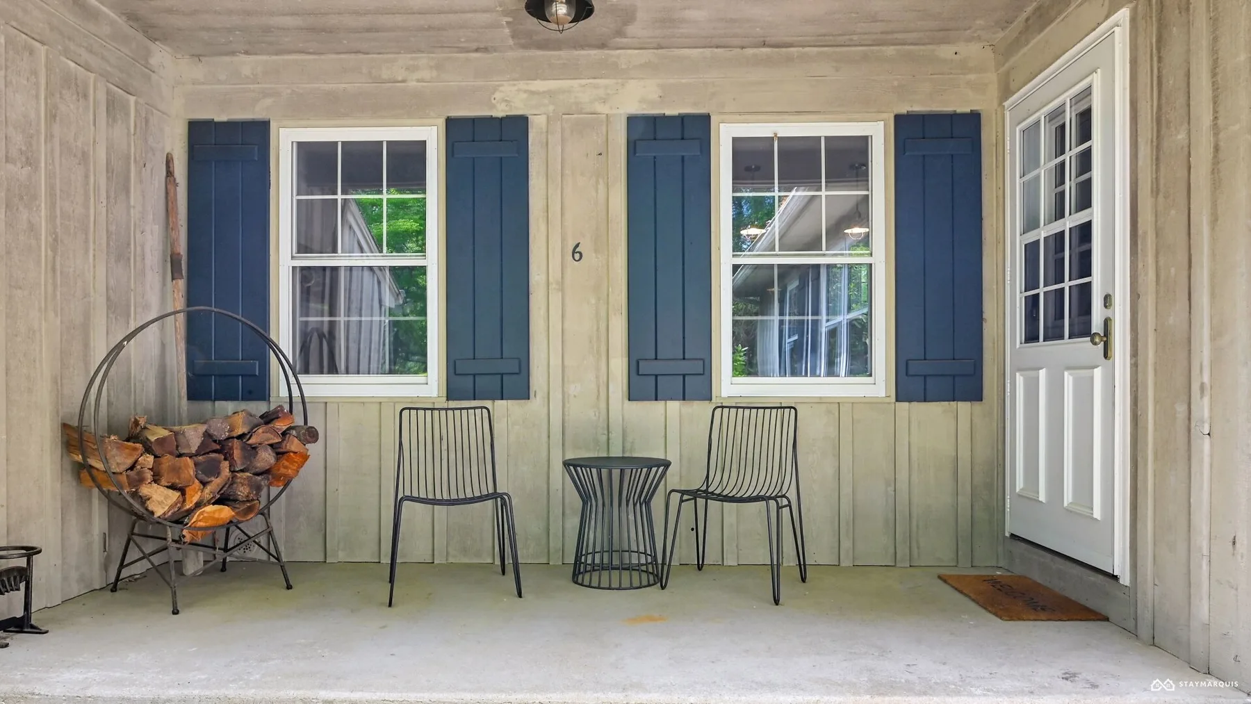 A covered porch with shuttered windows, metal seating, and a white door.
