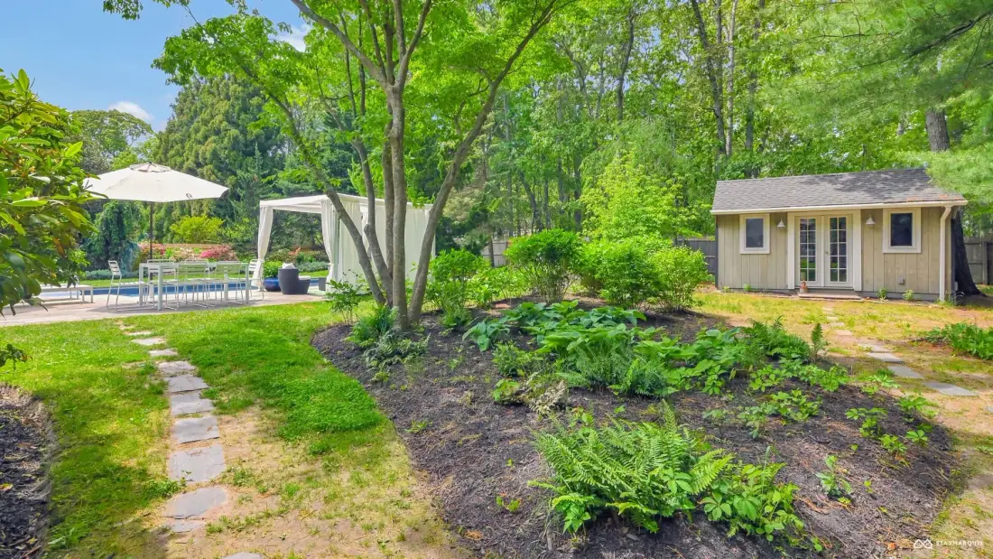 A landscaped garden path leads toward a small cottage beside a swimming pool.