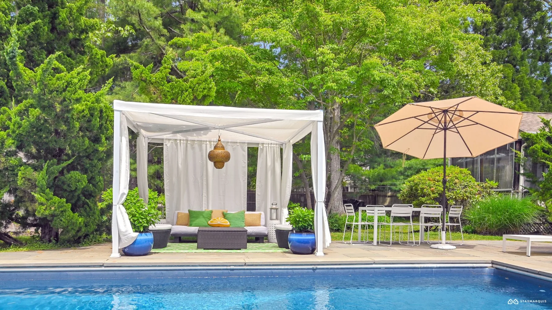 A poolside cabana with seating sits beside an outdoor dining area.