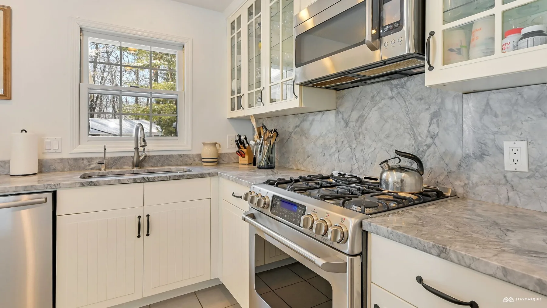 A bright kitchen with a gas range, stainless steel appliances, and glass-front cabinets.