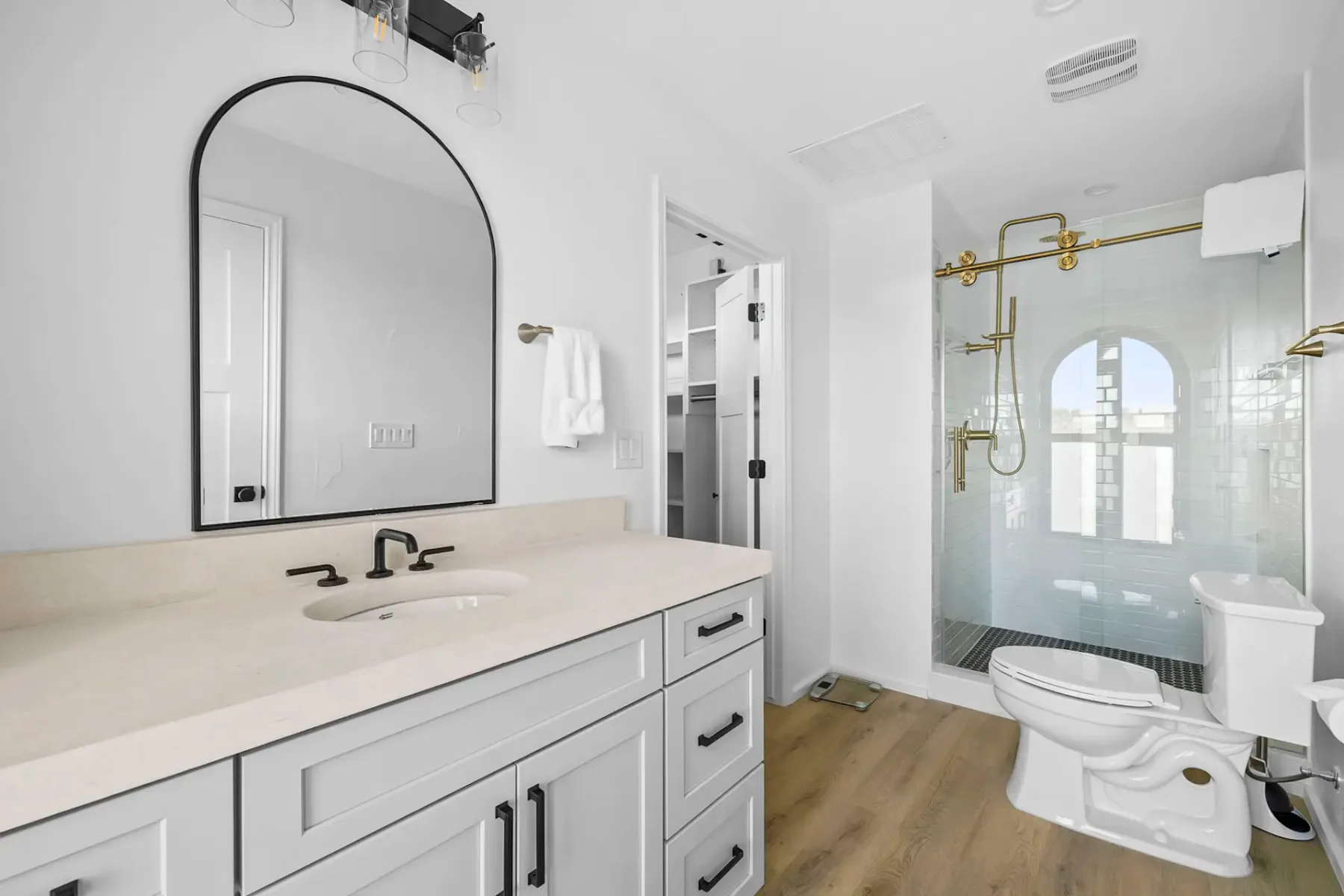 Un baño luminoso con lavabo blanco, espejo arqueado y ducha de vidrio.