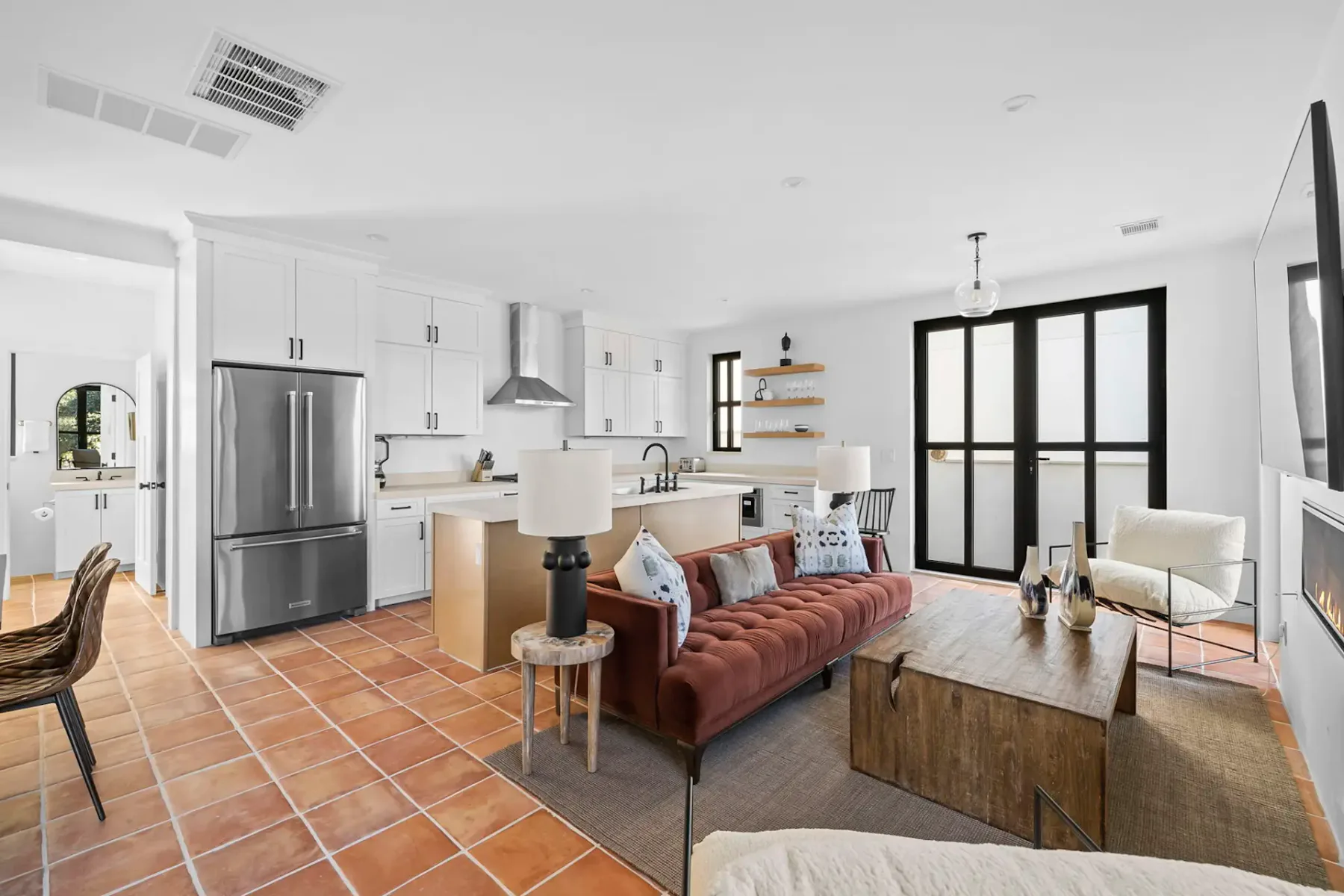An open-plan living room and kitchen with white cabinetry and a brick-red sofa.