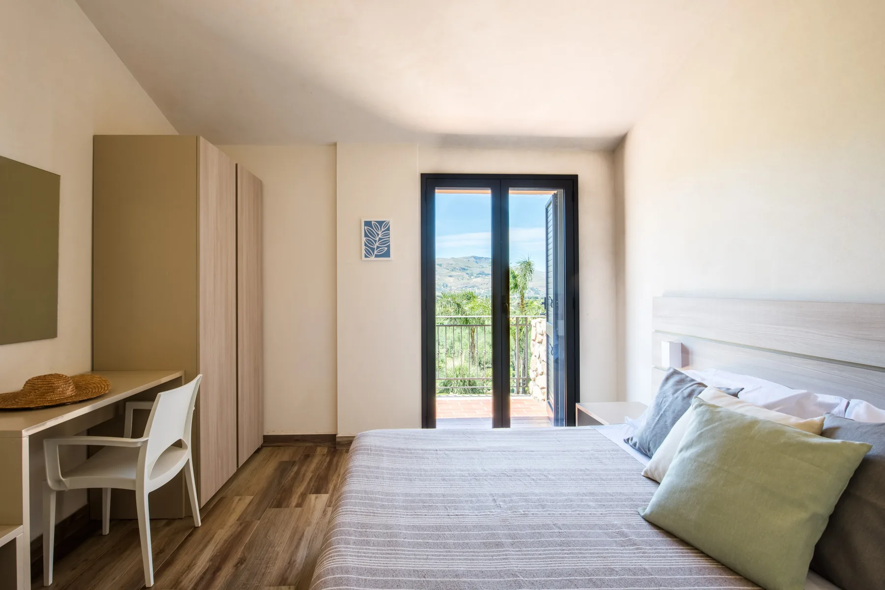 A bedroom with a bed, desk, and glass doors opening onto a balcony.