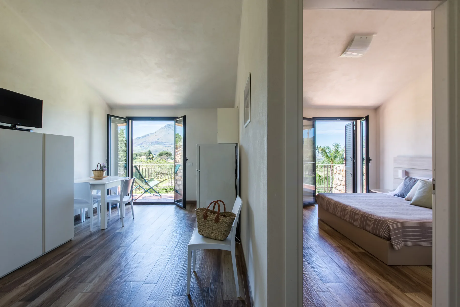A bright apartment interior with a dining area and a bedroom opening onto a balcony.