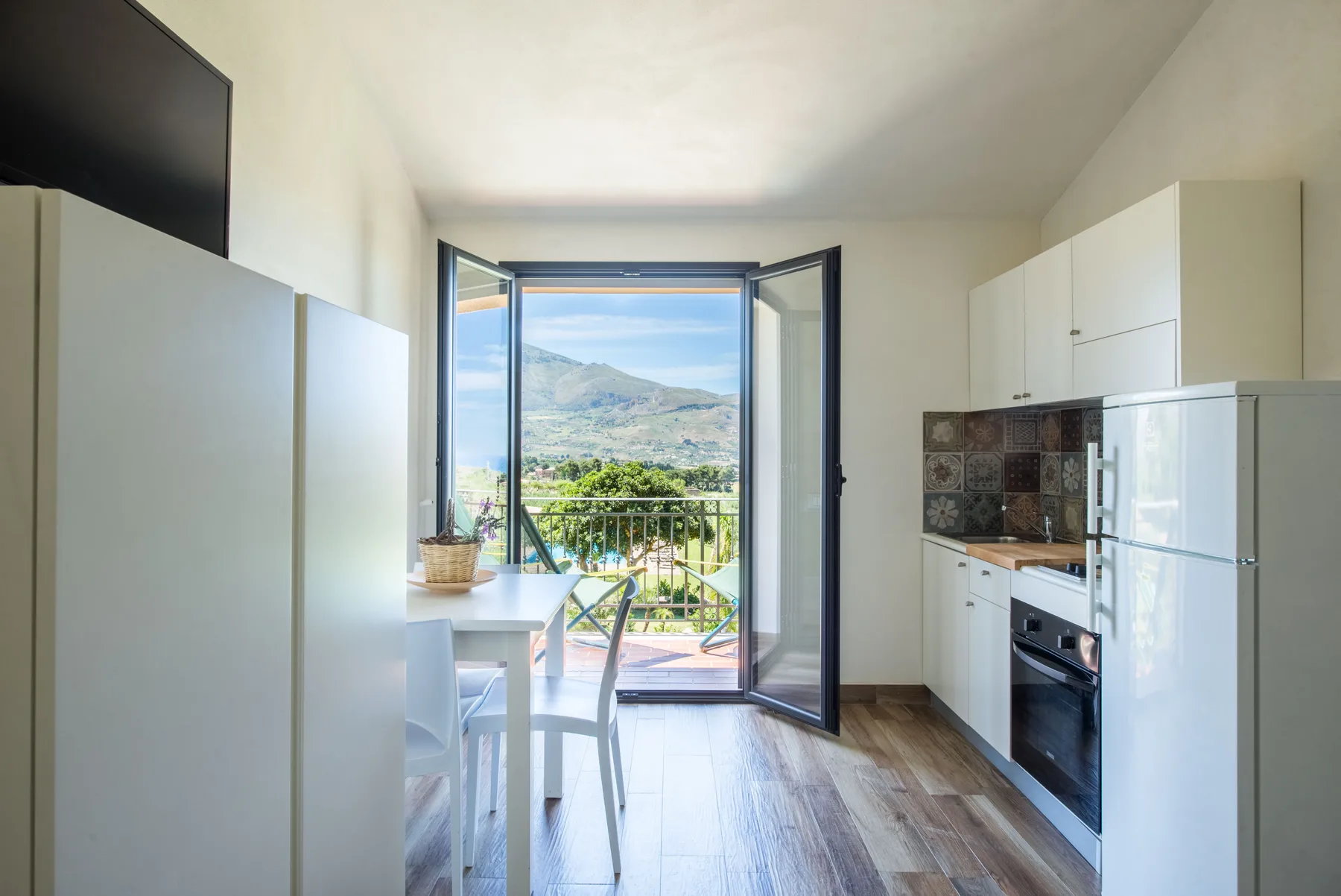 A bright kitchen opens onto a balcony with a view of the hills.