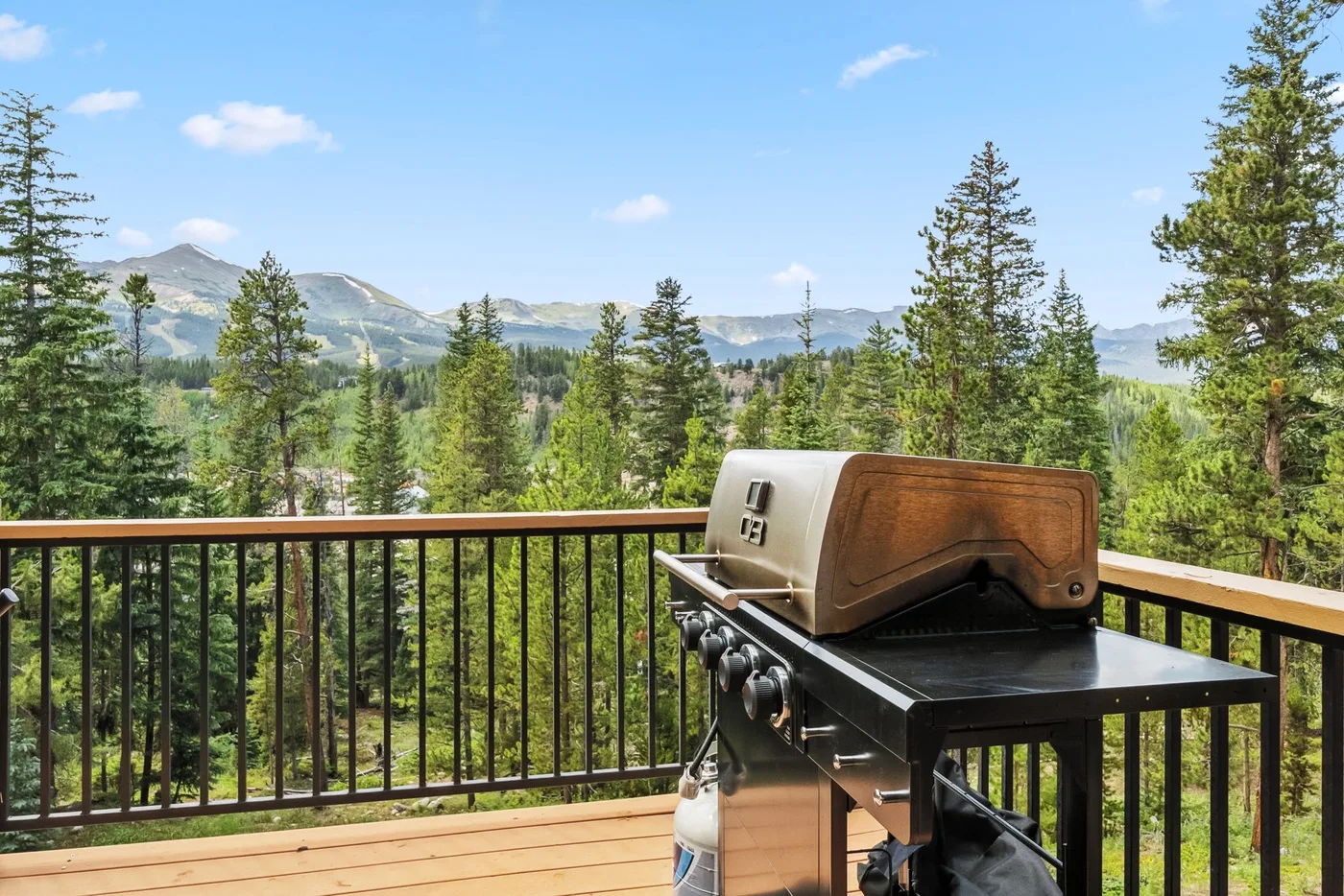 Una parrilla está en una terraza de madera con vistas a un paisaje montañoso y boscoso.