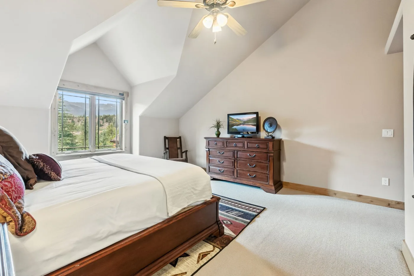 Un dormitorio luminoso con una cama, una cómoda de madera y una ventana grande.