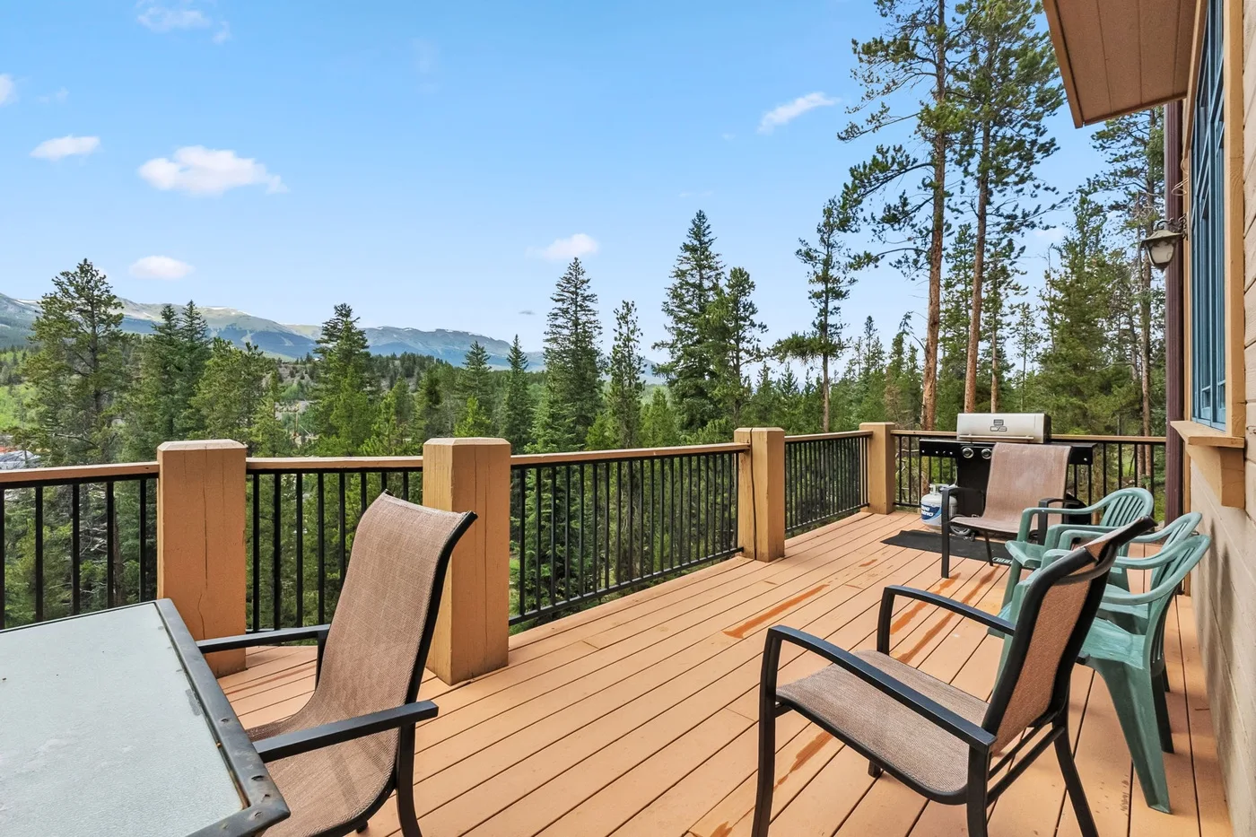 Una terraza de madera con asientos ofrece vistas de pinos y montañas lejanas.