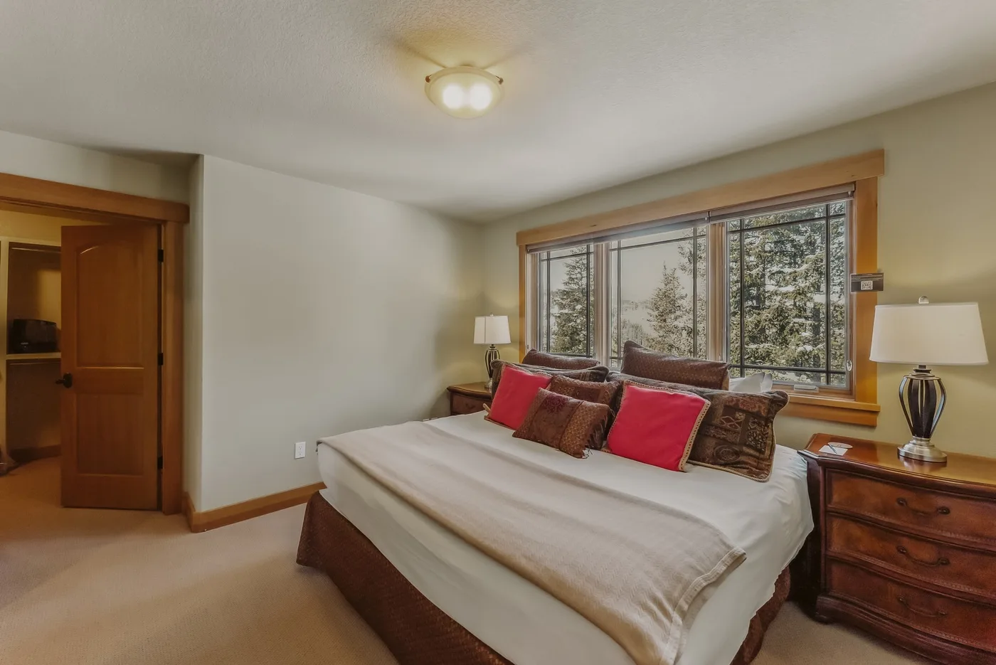 Un dormitorio con una cama grande bajo una ventana amplia con vista a los árboles.