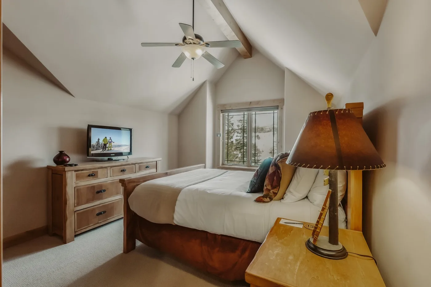 Un dormitorio con cama, cómoda y ventana bajo un techo inclinado.
