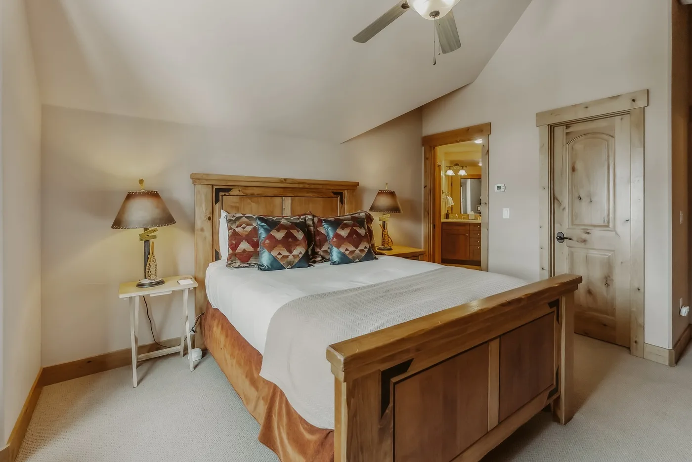 Un dormitorio con una cama de madera, cojines estampados y una mesita de noche.