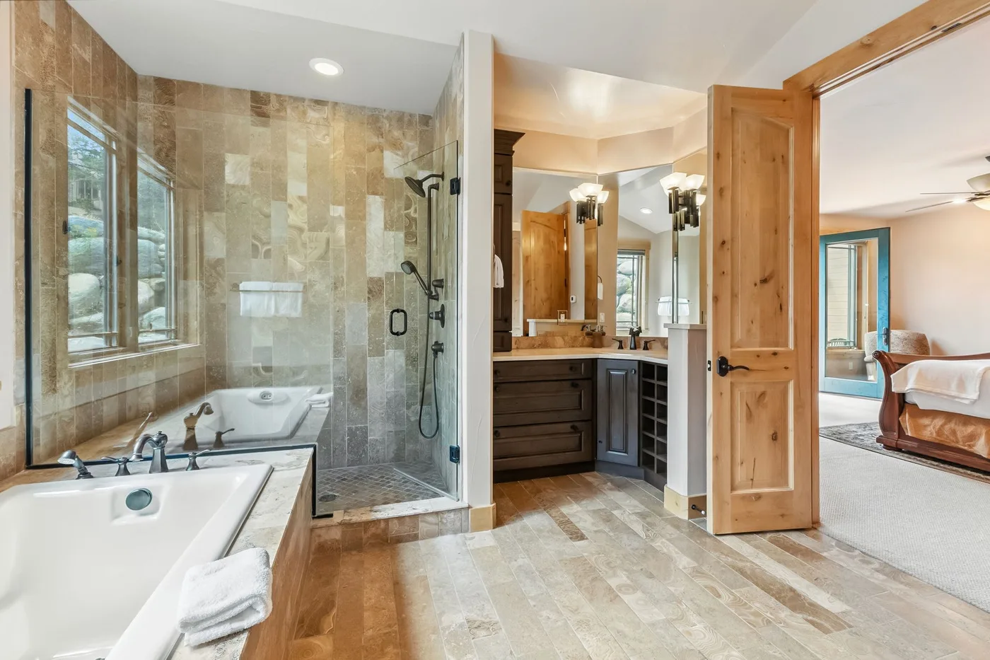 Un baño luminoso con bañera, ducha de vidrio y tocador junto a una puerta de madera abierta.